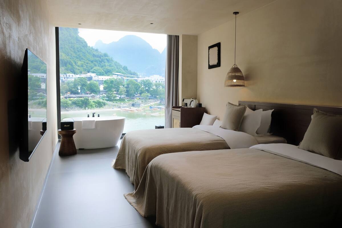 Habitación de hotel con dos camas, una bañera, un televisor y vistas a un paisaje montañoso.