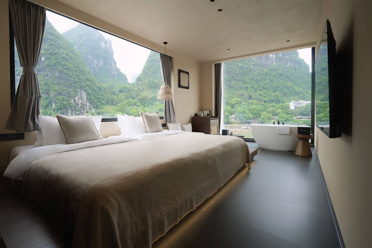Habitación de hotel moderna con una cama grande, una bañera y vistas a un paisaje montañoso.
