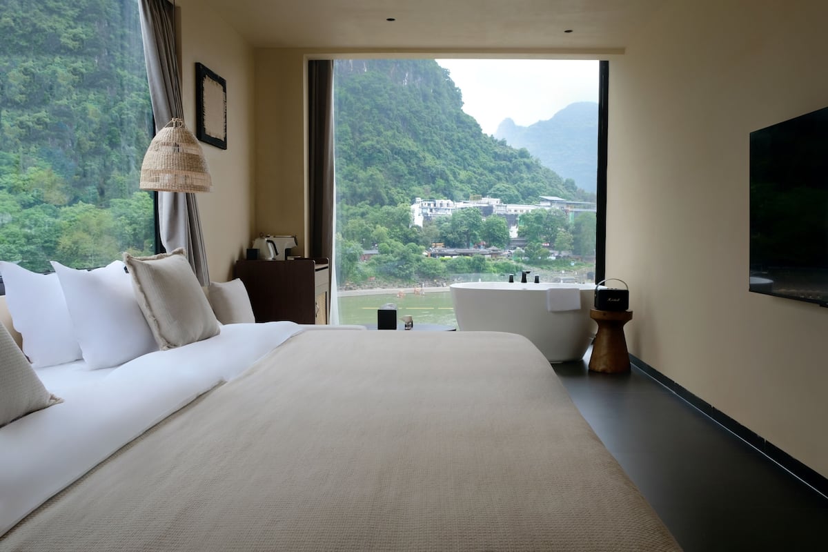 Un dormitorio con una cama grande, una bañera, un televisor y vistas a un paisaje montañoso.