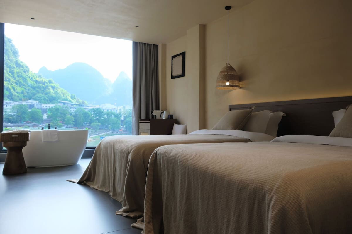 Habitación de hotel con dos camas, una bañera y vistas a un paisaje montañoso.