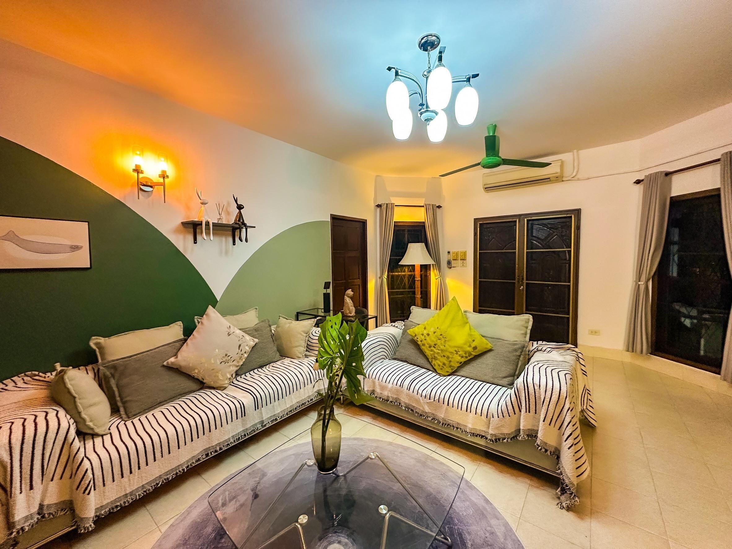 A living room with two striped sofas, a glass coffee table, and a green wall.
