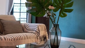 A living room with a striped sofa, a glass coffee table, and a large plant in a vase. - Kesorn Charming Authentic Thai Pool Villa Phuket (Rawai)