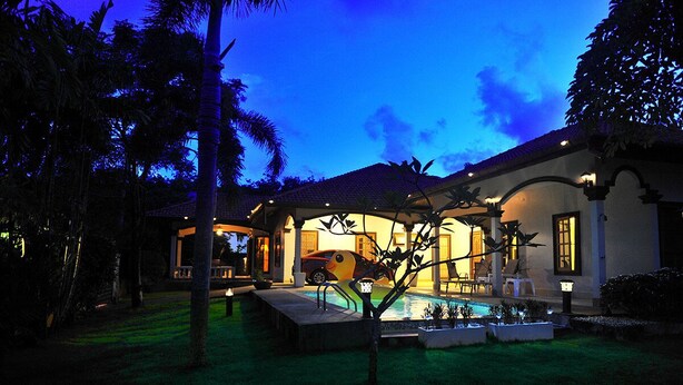 A poolside area with a swimming pool, palm trees, and a house with a tiled roof and arched windows. - Kesorn Charming Authentic Thai Pool Villa Phuket (Rawai)