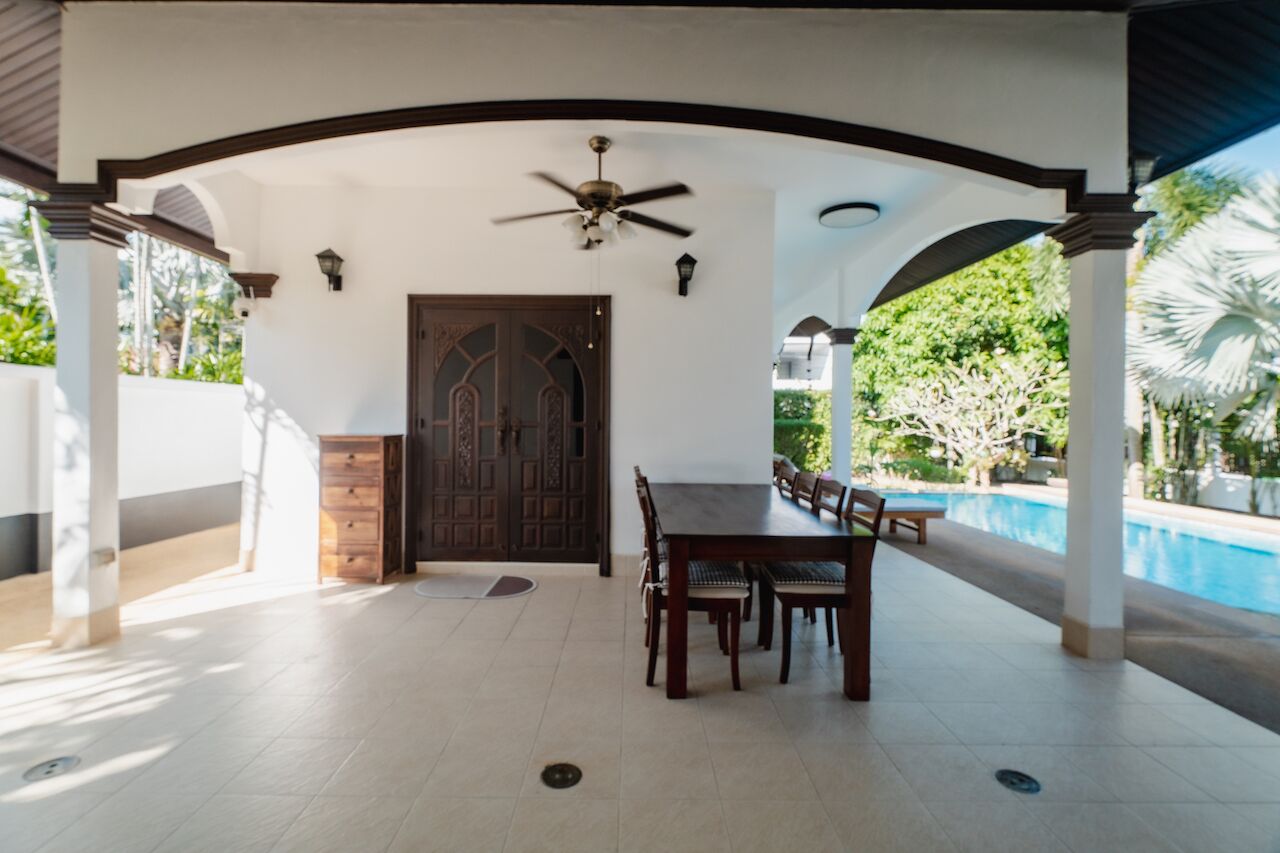 Un área de comedor al aire libre cubierta con una piscina al fondo.
