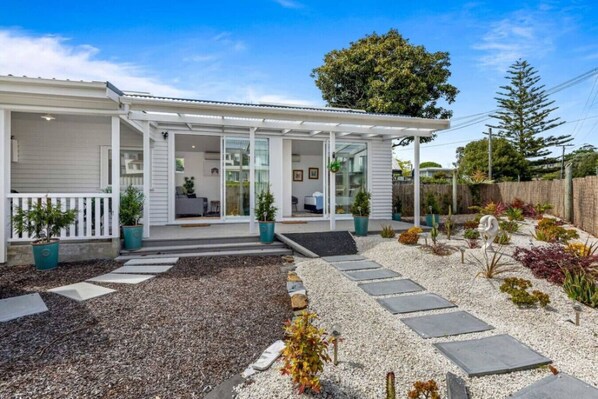 A modern house with a covered porch, a garden with gravel paths, and various plants.