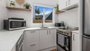 A modern kitchen with white cabinetry, a built-in microwave, a gas stove, and a stainless steel refrigerator. - Escape to Kohi Cottage - Your Beachside Haven (Auckland)