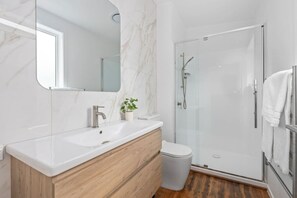 Een moderne badkamer met een marmeren wastafel, een houten wastafelmeubel en een douchecabine met glazen wanden.
