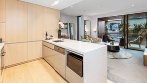 Eine moderne Küche mit einer zentralen Kochinsel, einem Essbereich mit einer Couch und Stühlen sowie einer großen Schiebeglastür, die auf einen Balkon führt.