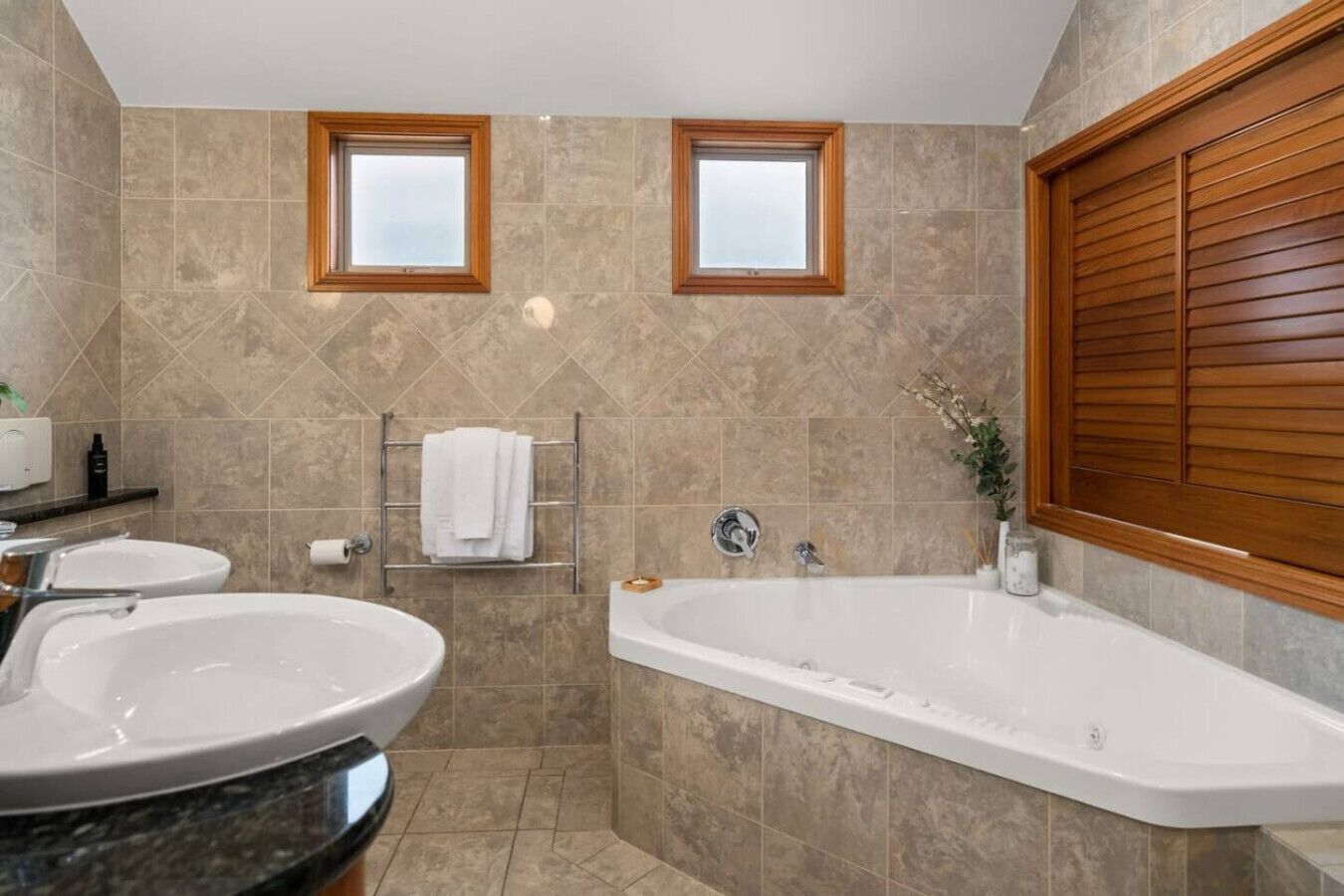 A bathroom with two sinks, a bathtub, and a window with wooden shutters.