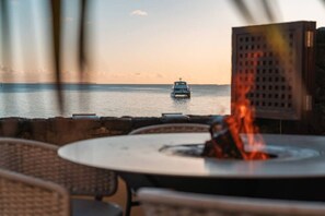 Blick auf ein Boot auf dem Wasser, eine Feuerstelle und Sitzgelegenheiten im Freien.