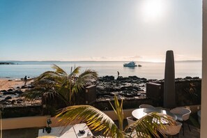 A balcony with a view of the sea, a boat in the distance, and a rocky beach. - Takapuna Beachfront w/Stunning Views (Auckland)