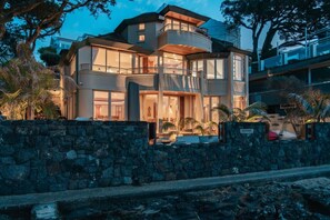 A modern multi-story house with a stone wall in front, large windows, and a balcony. - Takapuna Beachfront w/Stunning Views (Auckland)