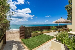 A patio area with a view of the ocean, a stone wall, and a seating area with an umbrella. - Takapuna Beachfront w/Stunning Views (Auckland)