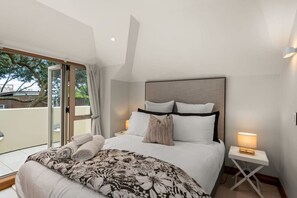 Een moderne slaapkamer met een groot bed, uitzicht op het omliggende landschap en een klein nachtkastje met een lamp.
