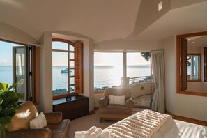 A spacious bedroom with a large bed, a seating area with a chair and sofa, and a balcony with a view of the sea. - Takapuna Beachfront w/Stunning Views (Auckland)