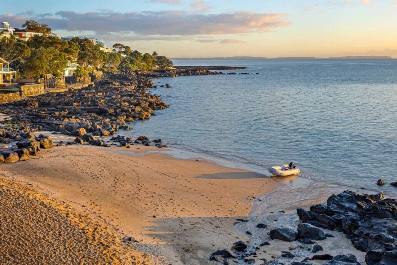 A beach with a rocky shoreline, a small boat, and buildings in the background.