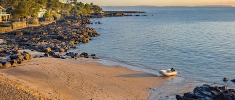 Una playa con costa rocosa, un barco pequeño y edificios al fondo.