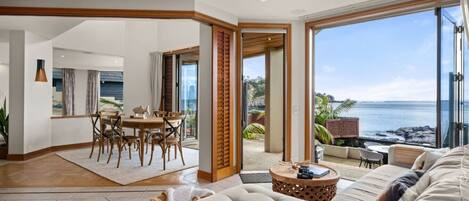 A spacious living area with a large sofa, a dining table with chairs, and a view of the ocean.