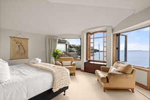 A bedroom with a bed, two armchairs, a sofa, a large window with a view of the sea, and a painting on the wall. - Takapuna Beachfront w/Stunning Views (Auckland)