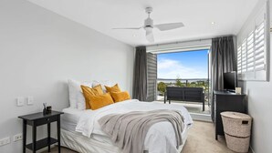 A modern bedroom with a bed, a small table, a TV, and a balcony with a view. - Ocean View Spacious 5BR Retreat for Families (Auckland)