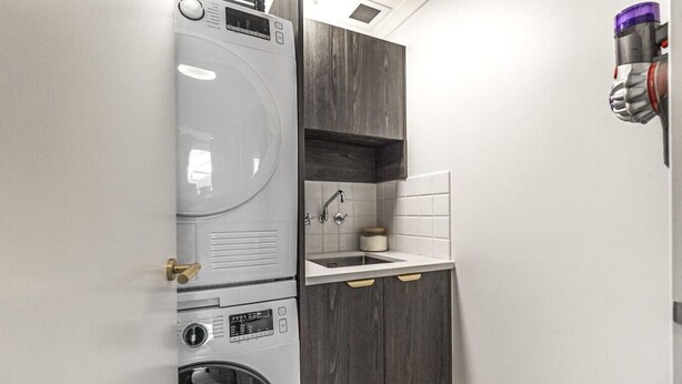 A compact laundry area with a washing machine, dryer, and a small sink with a cabinet above.