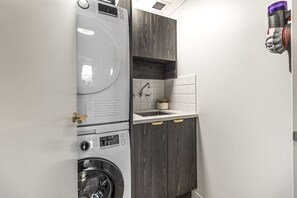 A compact laundry area with a washing machine, dryer, and a small sink with a cabinet above. - Luxurious Harbour View Apartment in Downtown (Auckland)
