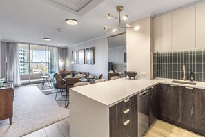 A modern kitchen with dark wood cabinets, a white countertop, and a dining area with a sofa and chairs. - Luxurious Harbour View Apartment in Downtown (Auckland)