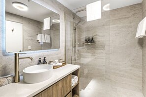 A modern bathroom with a large sink, a mirror, a shower, and a wooden vanity.