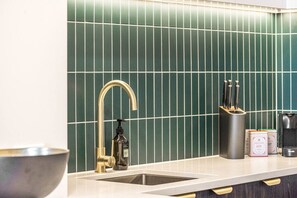 A kitchen with a modern design, featuring a stainless steel sink, a gold faucet, and a green tiled backsplash. - Luxurious Harbour View Apartment in Downtown (Auckland)