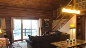 Een gezellig chalet binnen met houten vloer, een bank, een eettafel en een wenteltrap.