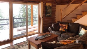 Een gezellig chaletinterieur met een houten trap, een leren bank en een boekenplank.