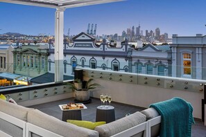 Une terrasse sur le toit offrant une vue panoramique sur la ville, un coin salon avec des coussins, une table avec un plateau de nourriture et une plante en pot.