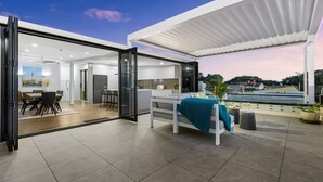 A modern open-plan living area with a dining space, kitchen, and a balcony with a view. - Stay Devonport - 3 Bedroom Penthouse (Auckland)
