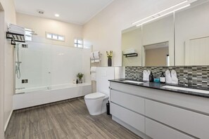 Un baño moderno con ducha envuelta en vidrio, inodoro blanco y tocador con un espejo grande.