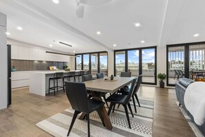 A modern kitchen with a central island, dining area with a large table and chairs, and a balcony with a view.