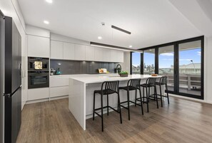 Une cuisine moderne dotée d’un îlot central, de tabourets de bar noirs et offrant une vue sur la ville grâce à de grandes fenêtres.