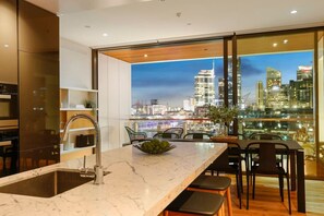 A modern kitchen with a large window overlooking a cityscape at dusk. - Harbour front Living at Wynyard Marina (Auckland)