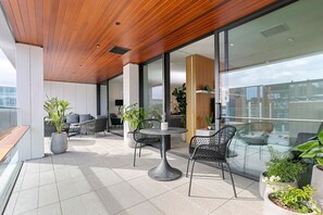 A modern outdoor lounge area with a wooden ceiling, glass walls, and a mix of seating options including chairs and a table. - Harbour front Living at Wynyard Marina (Auckland)