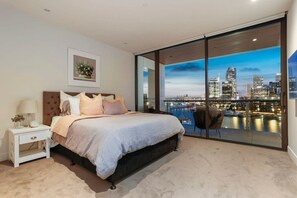 A bedroom with a bed, nightstand, and a view of a city skyline through large glass doors. - Harbour front Living at Wynyard Marina (Auckland)