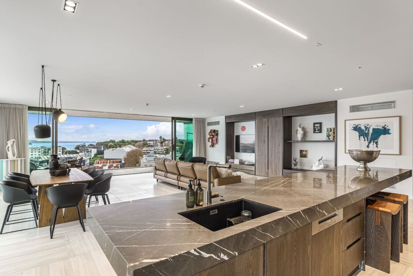 A modern kitchen with a marble countertop, a built-in sink, and a dining area with a view.