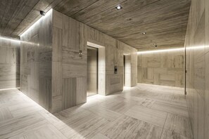 A modern elevator lobby with wood-paneled walls and floors, recessed lighting, and a minimalist design.