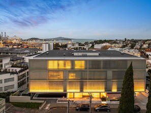 Un bâtiment moderne à la façade réfléchissante, entouré d’immeubles résidentiels et avec un port en arrière-plan.