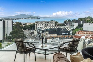 Una terraza con dos sillones de mimbre, una mesa de vidrio y vistas a un paisaje urbano y una masa de agua.