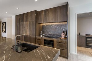 A modern kitchen with dark wood cabinetry, a marble countertop, and a built-in dishwasher.