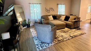 Ein geräumiges Wohnzimmer mit einem grauen Sessel, einem braunen Ecksofa und einem gemusterten Teppich.