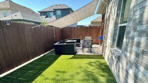 Ein Garten mit Kunstgrashalm, einem Holzzaun und einer Terrassenfläche mit Gartenmöbeln.