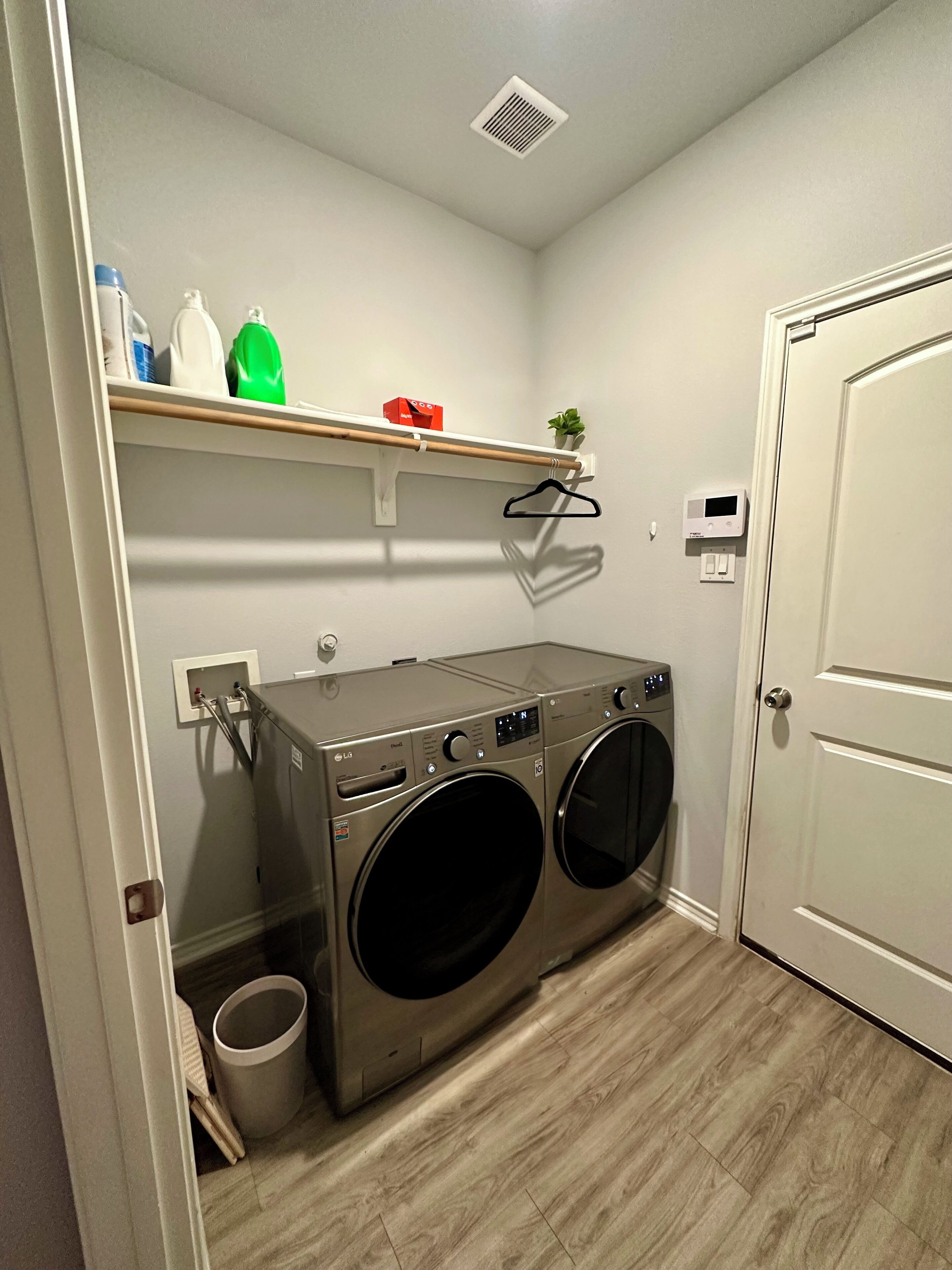 Un cuarto de lavado con dos lavadoras de carga frontal, un estante con productos de limpieza y una puerta.