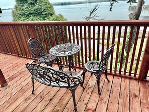 Een houten terras met een metalen tafel en stoelen, uitkijkend op een wateroppervlak.