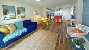 A living room with a blue sofa, a dining area with yellow chairs, a kitchen with white cabinets, and a ceiling fan. - NEW Amazing Sunshine-Up 6 Guests-Private Backyard (Port Orange)
