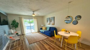 A modern living room with a blue sofa, yellow chairs, a white table with fruit, and a view to the outside. - NEW Amazing Sunshine-Up 6 Guests-Private Backyard (Port Orange)